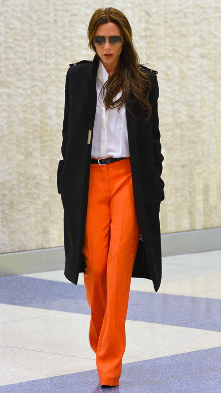 विक्टोरिया Beckham wearing orange pants, white top, and black trench coat