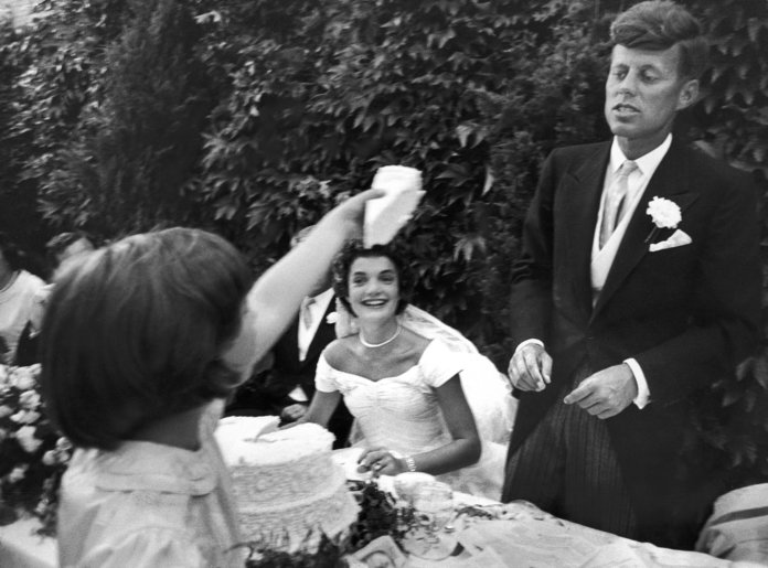 फूल girl Janet Auchincloss holds up a wedge of wedding cake for John F Kennedy 